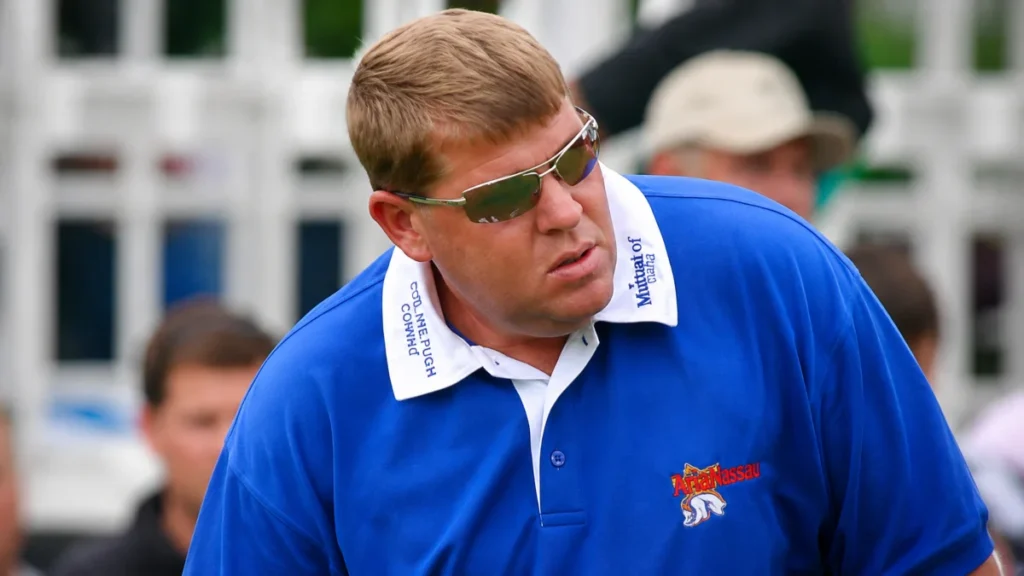 John Daly wearing a blue polo shirt and sunglasses at a golf event, featured in coverage of John Daly Net Worth and his golf career.