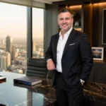 Misha Ezratti Net Worth featured in a luxury executive office wearing a formal business suit with a modern corporate background.
